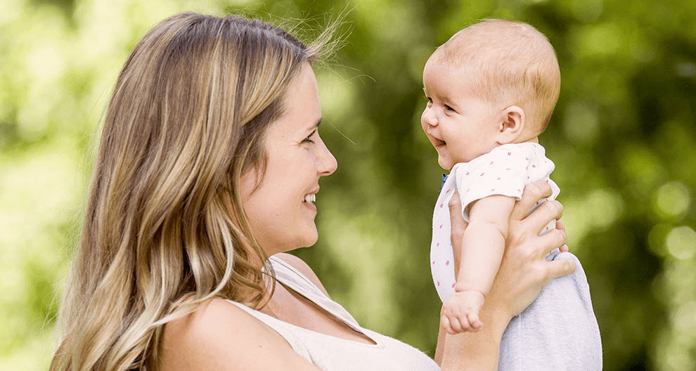A woman holds a baby outdoors.