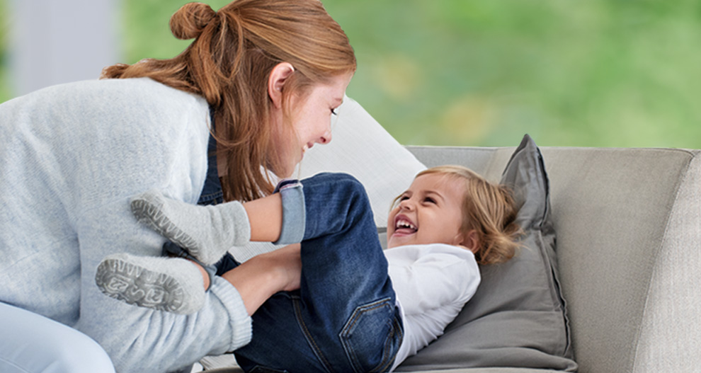A woman and a child are engaged in a playful interaction on a couch.