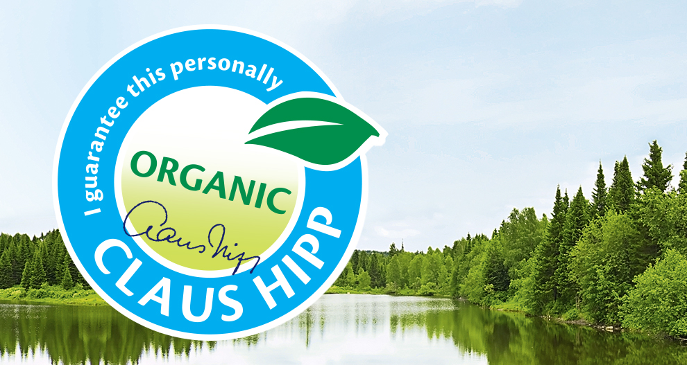 Un peisaj senin al unui lac înconjurat de copaci verzi și dese este suprapus cu un logo circular albastru mare pe care scrie "Garantez acest lucru personal" și "CLAUS HIPP" cu un simbol de frunze verzi și o semnătură.