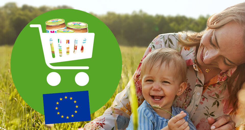 O femeie și un copil stau pe un câmp, cu un cărucior de cumpărături care conține borcane de mâncare pentru copii și steagul Uniunii Europene.