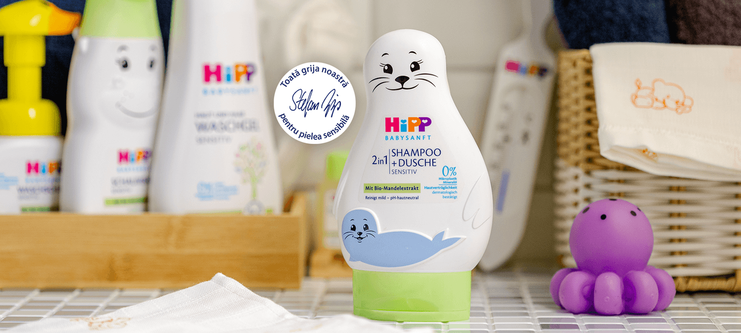 O sticlă albă de șampon cu un design de sigiliu și o caracatiță de jucărie mov sunt expuse în mod vizibil pe un raft de baie, înconjurate de alte produse de îngrijire pentru copii.